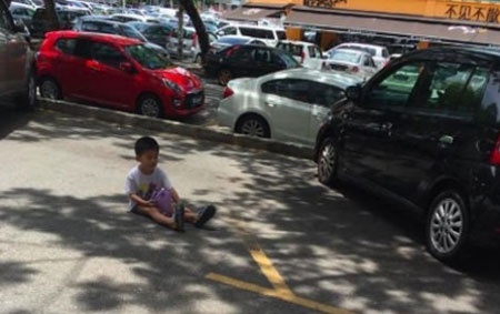 Cậu bé ngồi giữa trưa nắng giữ chỗ đỗ xe cho mẹ. Ảnh: Thestar.